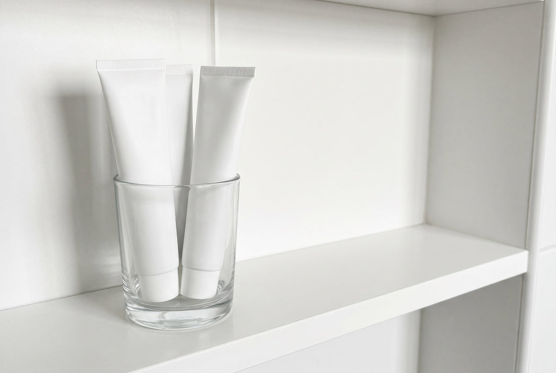 Three unbranded white toothpaste tubes in a glass on a clean bathroom shelf