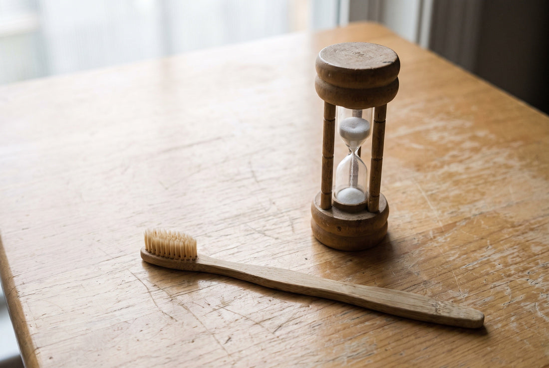 Sand timer next to a toothbrush on a wooden surface in daylight