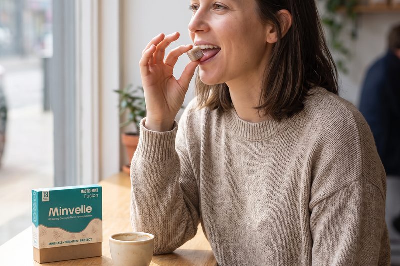 A woman at a cafe window placing a piece of Minvelle gum in her mouth